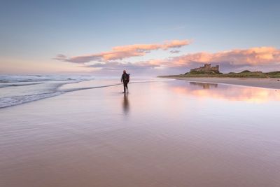 Rear view of man standing at beach against sky during sunset