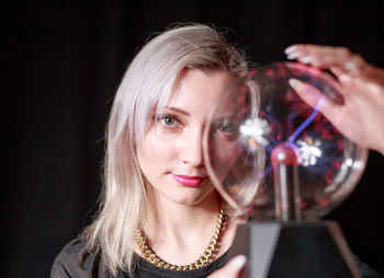 Close-up portrait of young woman holding plasma ball over black background