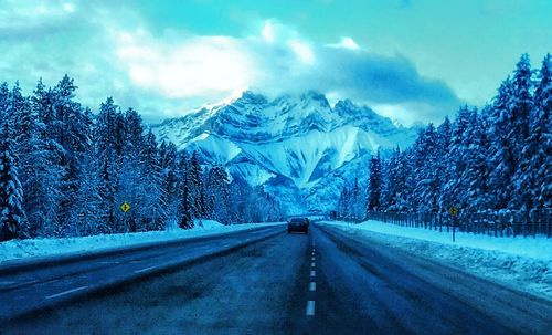 Road by snowcapped mountain against sky during winter