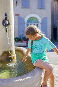 Girl looks at the water of old fountain on the typical square of small european villages, travel