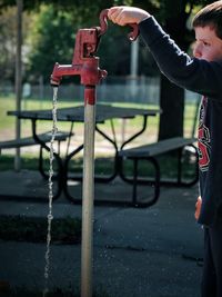 Cropped image of boy holding tap while standing in park