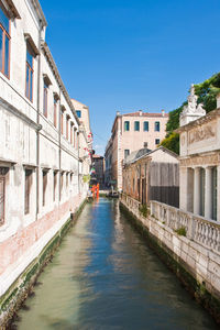 Canal amidst buildings against clear blue sky