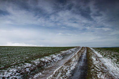 Empty road amidst field against sky