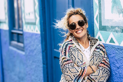 Portrait of smiling woman wearing sunglasses standing by door