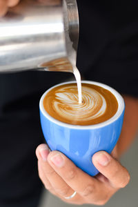 Close-up of hand pouring milk in coffee