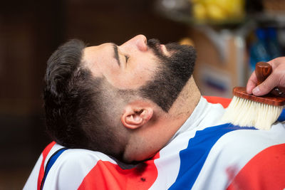 Cropped hand of barber cleaning hair on customer cape in salon