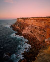 Scenic view of cliff by sea against sky during sunset