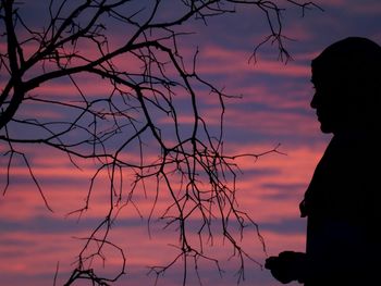 Side view of silhouette woman standing by bare tree against sky during sunset