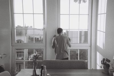 Rear view of shirtless man standing against window at home