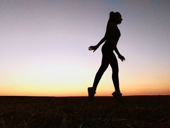 Silhouette woman walking on field against clear sky during sunset