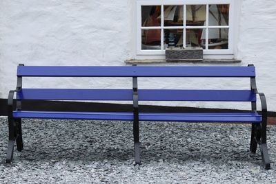 Empty bench in park by building during winter