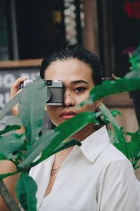 Portrait of young woman with camera seen through plant