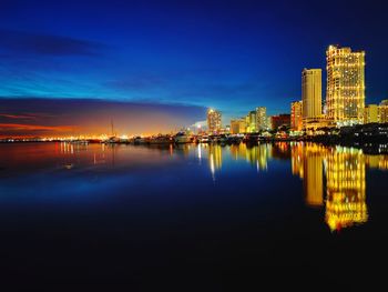 Illuminated buildings by river against sky at night