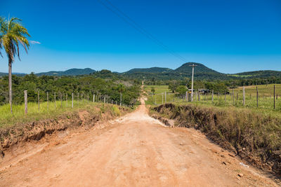 Dirt road amidst field against blue sky