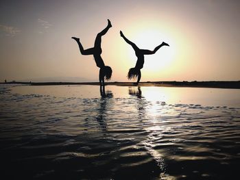 Silhouette young women practicing handstand on shore