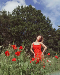 Woman standing by red poppy flowers on field