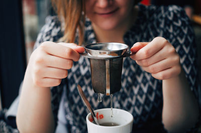 Midsection of young woman holding infuser over tea cup at restaurant