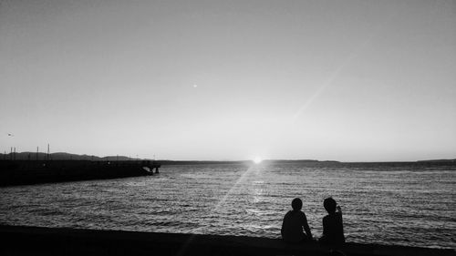 Silhouette people standing by sea against clear sky