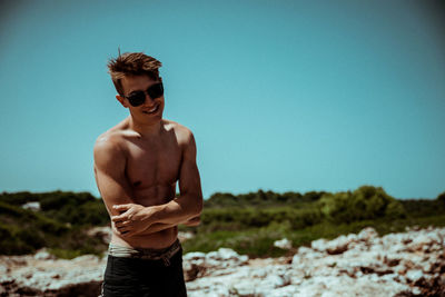 Shirtless young man standing at beach against clear sky