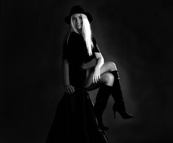 Portrait of smiling young woman wearing hat sitting against black background