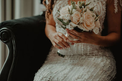 Midsection of bride holding bouquet while sitting on chair