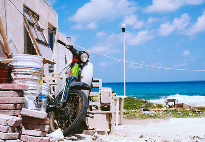 Abandoned motorcycle parked at beach against sky