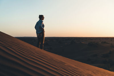 Man standing on sand dune in desert against sky