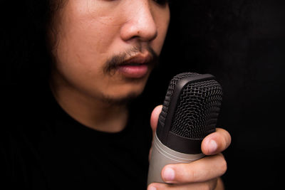 Close-up of young singer holding microphone against black background