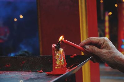 Cropped hand of man holding burning candles in temple