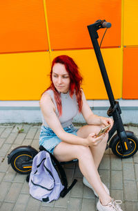 Woman uses a smartphone and an electric scooter in the summer in the city