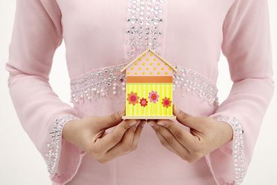 Midsection of woman holding model home against white background