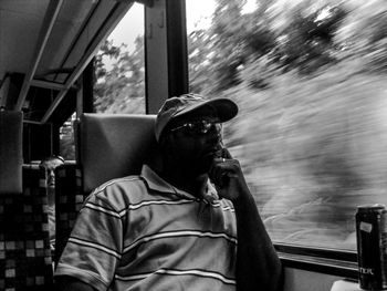 Side view of man wearing sunglasses sitting in train coach. 