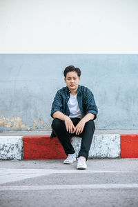 Portrait of young man sitting against wall