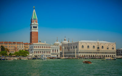 View of buildings by canal against clear blue sky