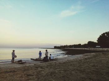 People playing on beach against sky during sunset