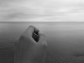 Cropped image of hand against sea at beach