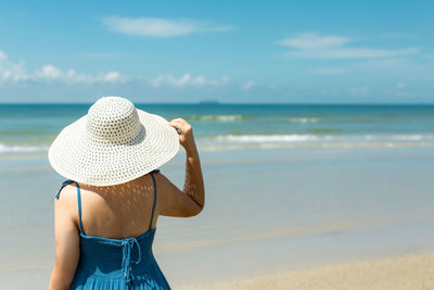 Rear view of woman wearing hat at beach against sky