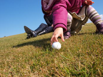 Low section of child holding golf ball on grassy field against clear blue sky