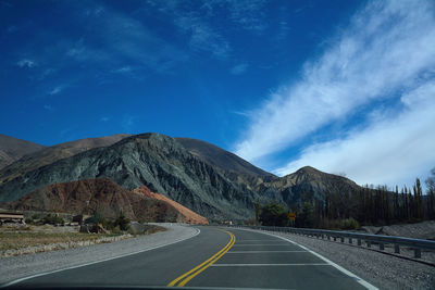 Empty road by mountain against blue sky