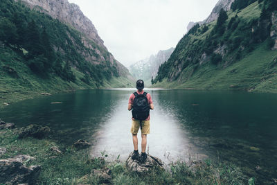 Rear view of man standing by lake and mountains