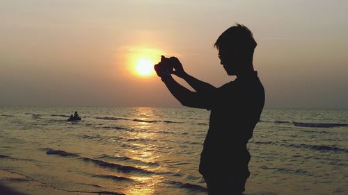 Silhouette man photographing at beach during sunset