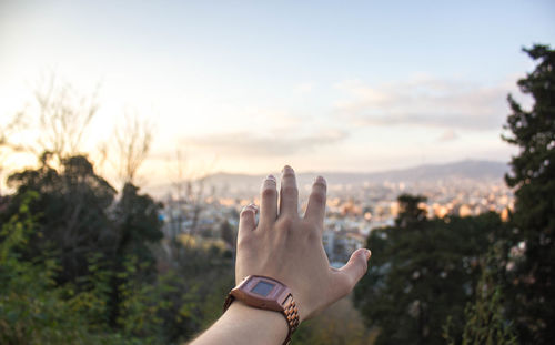 Cropped image of hand against residential district and sky during sunset