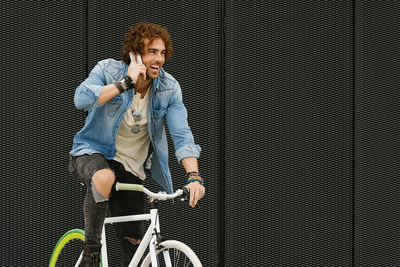 Man with mobile phone while cycling against building