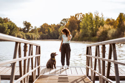 Rear view of woman sitting on railing against sky