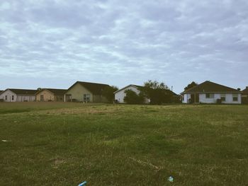 Houses on grassy field against cloudy sky