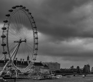 Ferris wheel in city against cloudy sky