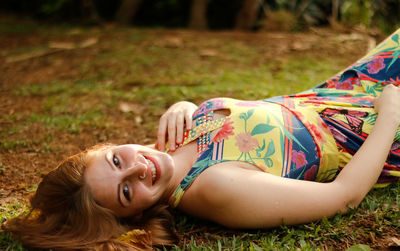 Portrait of smiling young woman lying on field at park