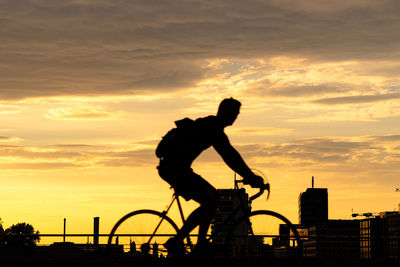 Silhouette man standing by bicycle against sky during sunset