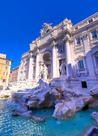 Low angle view of fountain and building against clear blue sky