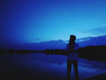 Silhouette man standing by lake against blue sky